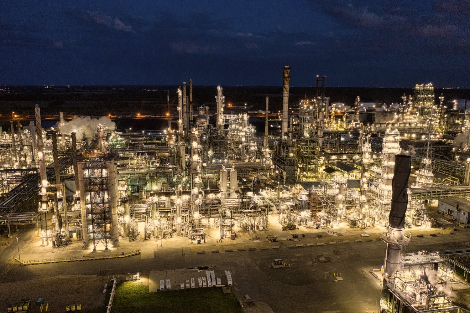An aerial view of a large process plant lit up at night, built out over many years.