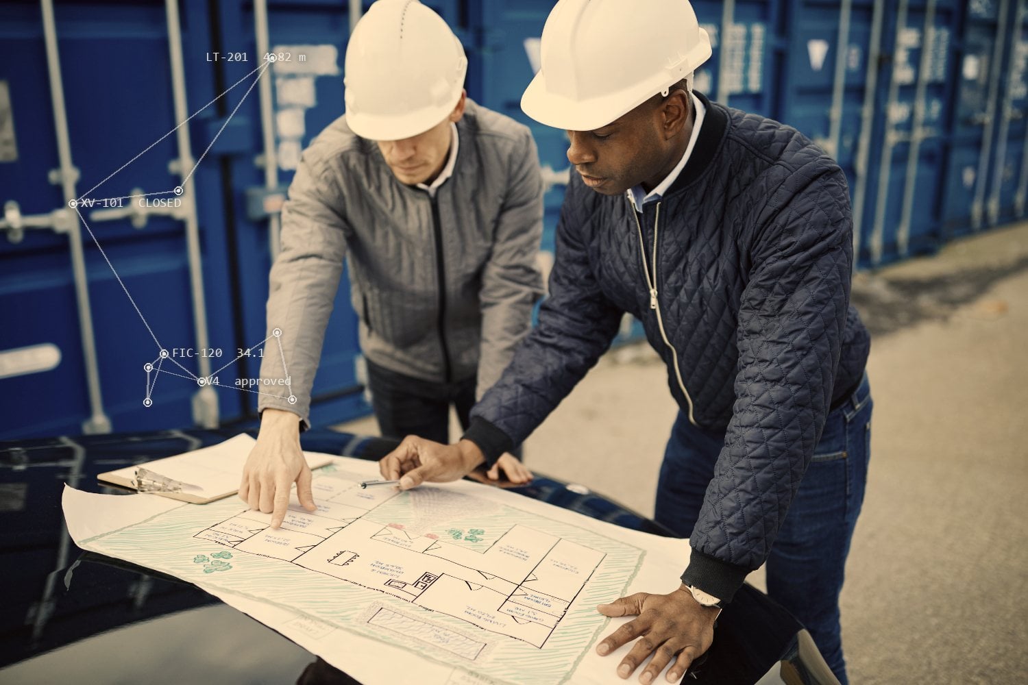 Two engineers in hard hats leaning over a printed drawing on site.